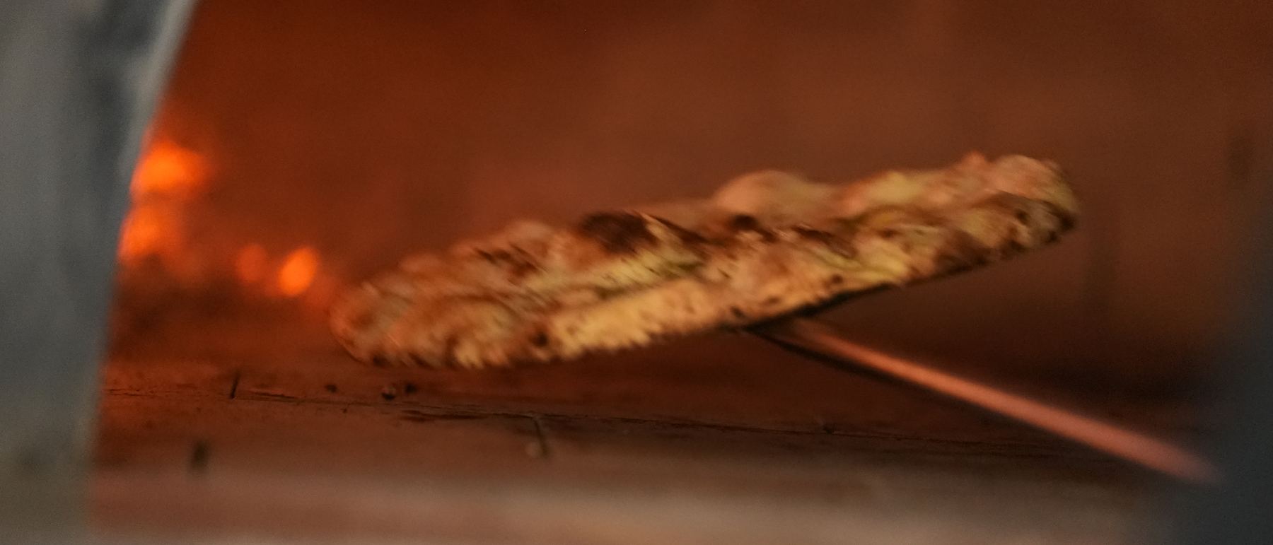 A pizza turning in the wood-fired oven